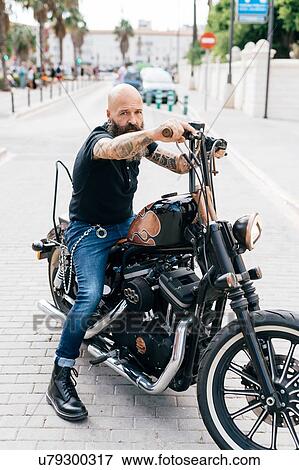Stock Photo - Portrait of mature male hipster astride motorcycle, Valencia, Spain. Fotosearch