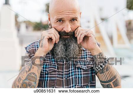 Stock Image - Portrait of mature male hipster pulling his moustache. Fotosearch
