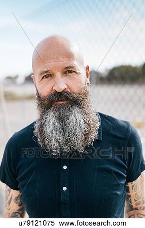 Stock Photography - Portrait of mature male hipster with grey beard in front of wire fence. Fotosearch