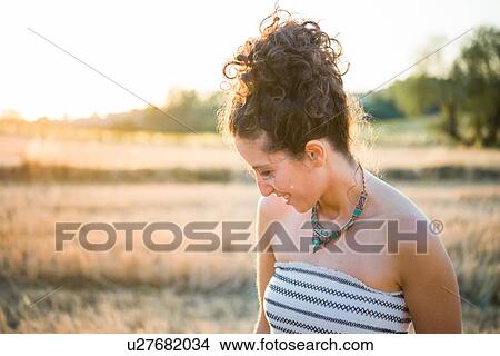 Picture - Portrait of mid adult woman, standing in field, looking down, smiling. Fotosearch