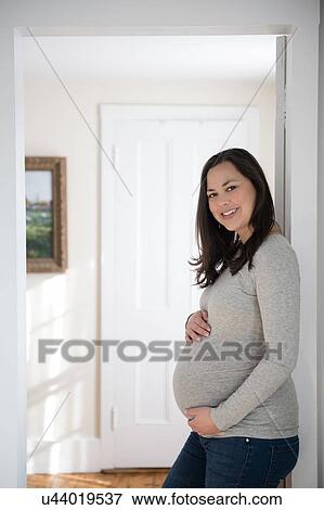 Stock Photo - Portrait of pregnant woman standing in doorway, touching belly. Fotosearch