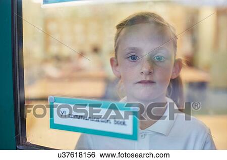 Stock Photograph - Portrait of schoolgirl looking through classroom window at primary school. Fotosearch
