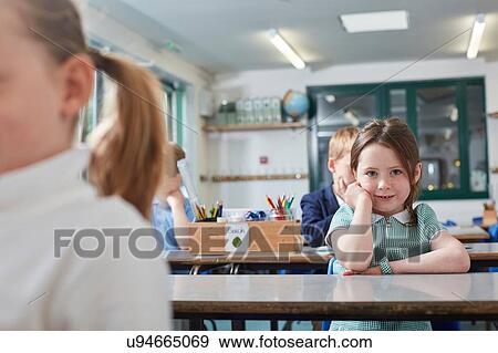 Stock Photo - Portrait of schoolgirl sitting at primary school classroom desk. Fotosearch