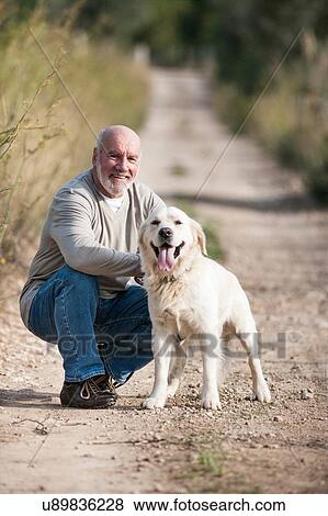 Stock Photo - Portrait of senior man crouching beside pet dog. Fotosearch