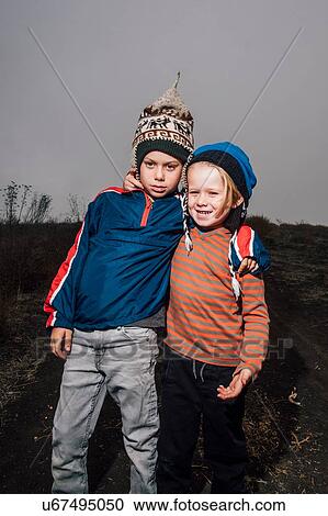 Stock Image - Portrait of two brothers, outdoors, wearing knitted hats, arms around each other. Fotosearch