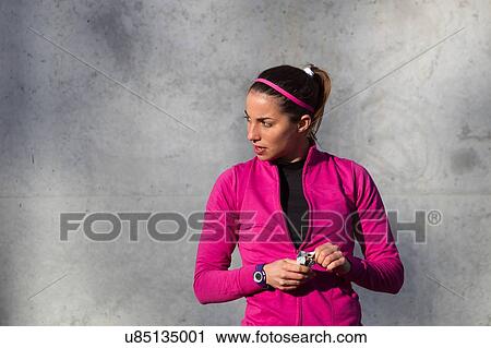 Stock Image - Portrait of woman holding protein bar looking away. Fotosearch