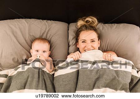Portrait of woman lying in bed under duvet with baby daughter, overhead view View Large Photo Image Stock Image - Portrait of woman lying in bed under duvet with baby daughter, overhead view. Fotosearch