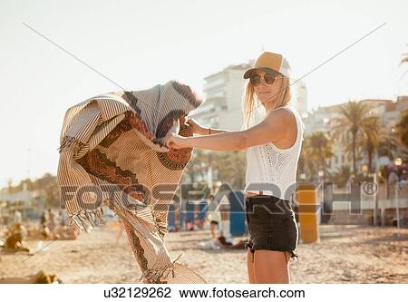 Stock Image - Portrait of woman on beach, unfolding picnic blanket, Sitges, Catalonia, Spain. Fotosearch