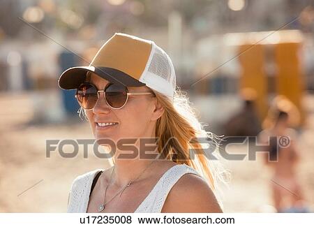 Stock Photo - Portrait of woman on beach, wearing sunglasses and cap, Sitges, Catalonia, Spain. Fotosearch