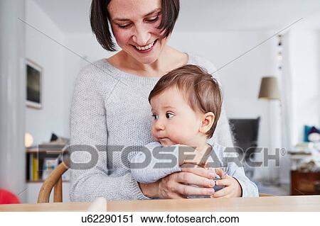 Stock Image - Portrait of woman sitting at table with baby daughter. Fotosearch
