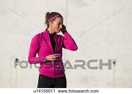 Stock Image - Portrait of woman wearing earphones holding smartphone. Fotosearch