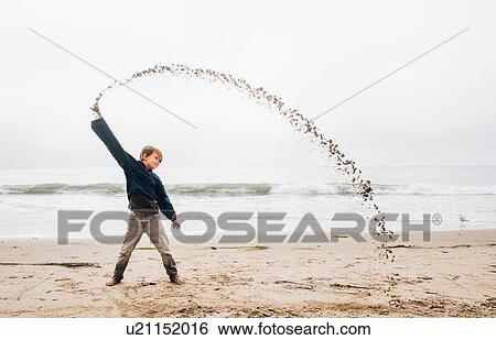 Portrait of young boy on beach, throwing sand in arch shape View Large Photo Image Stock Photograph - Portrait of young boy on beach, throwing sand in arch shape. Fotosearch