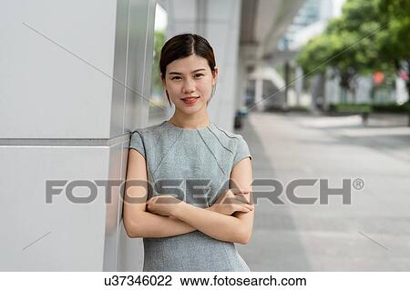 Stock Image - Portrait of young businesswoman leaning against wall in city, Shanghai, China. Fotosearch