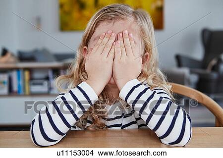 Portrait of young girl, sitting at table, covering face with hands View Large Photo Image Picture - Portrait of young girl, sitting at table, covering face with hands. Fotosearch