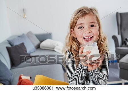 Portrait of young girl sitting in living room, holding glass of milk, smiling View Large Photo Image Stock Image - Portrait of young girl sitting in living room, holding glass of milk, smiling. Fotosearch