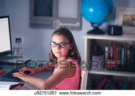 Portrait of young girl wearing glasses, sitting at desk, using computer View Large Photo Image Stock Photo - Portrait of young girl wearing glasses, sitting at desk, using computer. Fotosearch