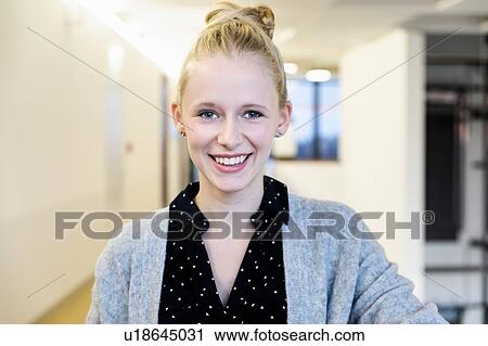 Stock Image - Portrait of young happy businesswoman in office corridor, head and shoulders. Fotosearch