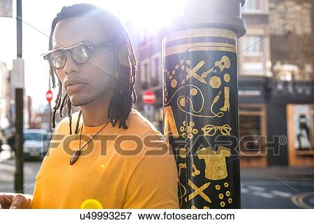 Stock Photo - Portrait of young man in street, leaning against lamppost. Fotosearch