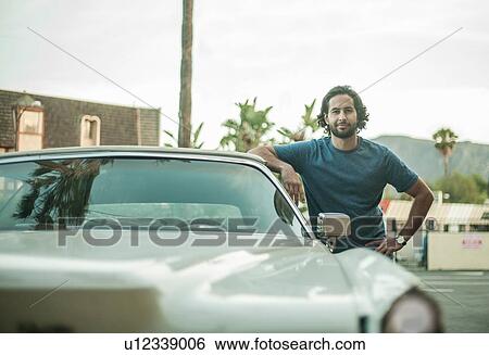 Stock Photograph - Portrait of young man, leaning on car, smiling. Fotosearch