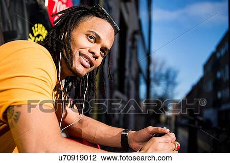 Portrait of young man outdoors, wearing earphones, smiling View Large Photo Image Stock Image - Portrait of young man outdoors, wearing earphones, smiling. Fotosearch