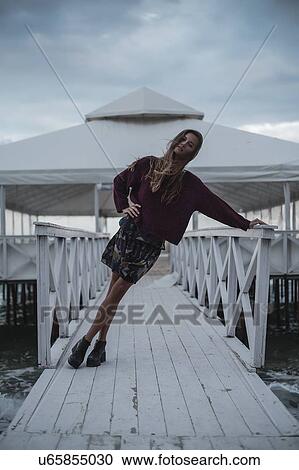 Stock Image - Portrait of young woman leaning sideways on pier at dusk, Odessa Oblast, Ukraine. Fotosearch