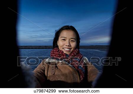 Stock Photo - Portrait of young woman taking selfie on beach at dusk, Tarragona, Catalonia, Spain. Fotosearch