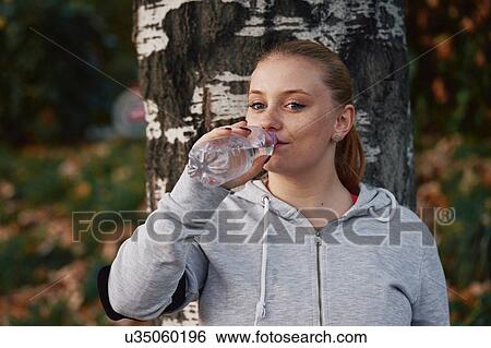 Stock Photograph - Portrait of young woman training in park drinking bottled water. Fotosearch