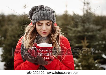 Stock Image - Portrait of young woman with coffee in christmas tree forest. Fotosearch