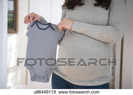Stock Photo - Pregnant woman holding infant bodysuit. Fotosearch