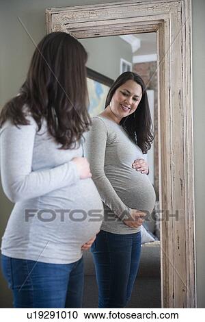 Pregnant woman looking in mirror, touching belly View Large Photo Image Stock Image - Pregnant woman looking in mirror, touching belly. Fotosearch