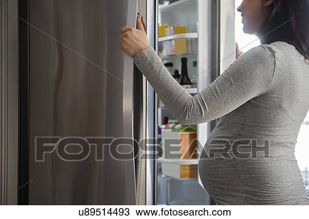 Stock Image - Pregnant woman looking into refrigerator. Fotosearch