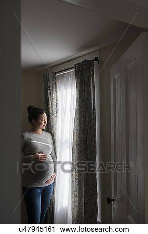 Stock Image - Pregnant woman looking through window. Fotosearch