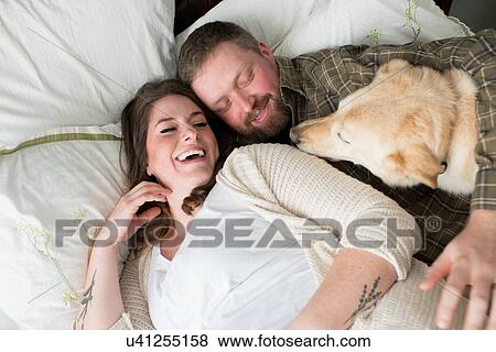 Pregnant woman lying with partner on bed, dog lying on bed beside them, elevated view View Large Photo Image Stock Photo - Pregnant woman lying with partner on bed, dog lying on bed beside them, elevated view. Fotosearch