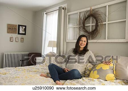 Stock Image - Pregnant woman sitting on bed. Fotosearch