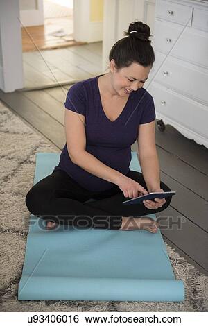 Pregnant woman sitting on yoga mat and using tablet pc View Large Photo Image Stock Photograph - Pregnant woman sitting on yoga mat and using tablet pc. Fotosearch