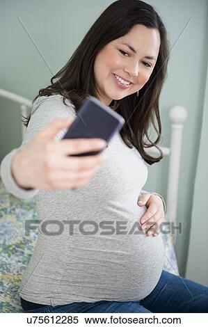 Stock Photography - Pregnant woman taking selfie with smart phone. Fotosearch