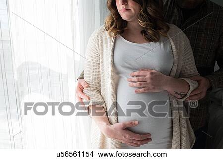 Pregnant woman touching stomach, man standing behind her showing affection, mid section View Large Photo Image Picture - Pregnant woman touching stomach, man standing behind her showing affection, mid section. Fotosearch