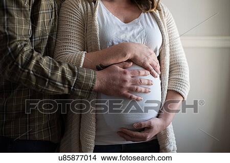 Pregnant woman touching stomach, partner showing affection, mid section View Large Photo Image Picture - Pregnant woman touching stomach, partner showing affection, mid section. Fotosearch