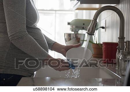 Pregnant woman washing bowl in kitchen sink, mid section View Large Photo Image Picture - Pregnant woman washing bowl in kitchen sink, mid section. Fotosearch