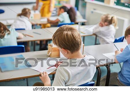 Stock Image - Primary schoolboy and girls doing schoolwork at classroom desks, rear view. Fotosearch