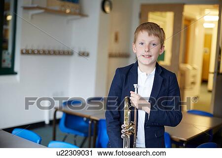 Stock Image - Primary schoolboy holding trumpet in classroom, portrait. Fotosearch