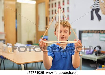 Stock Photography - Primary schoolboy holding up plastic straw pyramid in classroom. Fotosearch