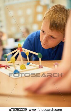 Primary schoolboy looking at plastic straw model on classroom desks View Large Photo Image Stock Photo - Primary schoolboy looking at plastic straw model on classroom desks. Fotosearch