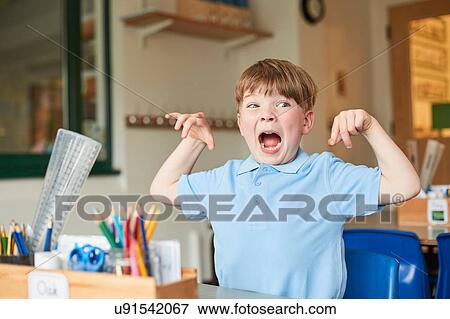 Stock Photo - Primary schoolboy mimicking monster in classroom. Fotosearch