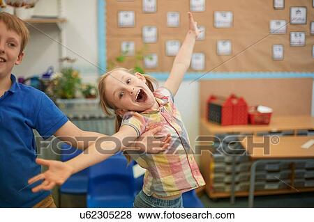 Stock Photo - Primary schoolgirl and boy fooling around in classroom. Fotosearch
