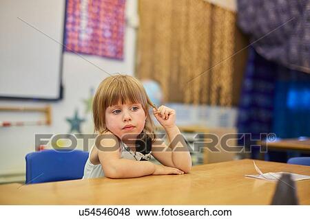 Stock Photo - Primary schoolgirl fiddling with hair at classroom desk. Fotosearch