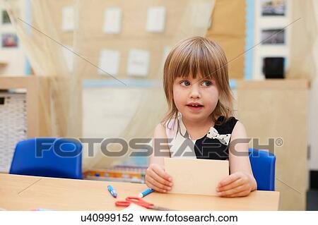Stock Image - Primary schoolgirl looking sideways from classroom desk. Fotosearch