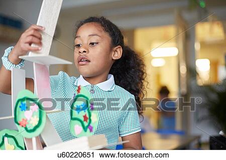 Stock Image - Primary schoolgirl making cardboard model in classroom. Fotosearch