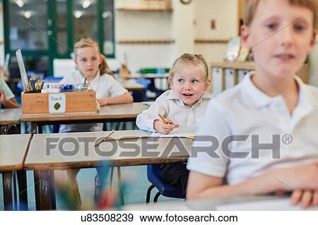 Stock Photo - Primary schoolgirls and boy doing schoolwork at classroom desks. Fotosearch