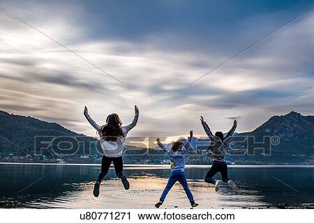 Rear view of boy and young women jumping mid air by river at dusk, Vercurago, Lombardy, Italy View Large Photo Image Stock Image - Rear view of boy and young women jumping mid air by river at dusk, Vercurago, Lombardy, Italy. Fotosearch